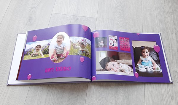 a photobook showing a page with birthday pictures of a one year old baby girl on a purple background with pink balloons